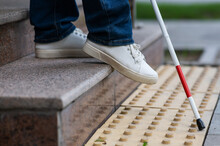 Close-up Of Female Foot, Walking Stick And Tactile Tiles. Blind Woman Walking Down Stairs Using A Cane. 