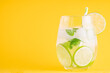 Summer lemonade with basil and lime on yellow background. One fresh summer cocktail with basil, green lemon and ice cubes. Drink concept
