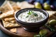Tzatziki sauce in a ceramic bowl, surrounded by pita bread triangles, olives, and feta cheese