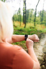 Wall Mural - Portrait of a happy active beautiful senior caucasian woman runner running while checking heart rate at park, female in sport cloth jogging while looking on watch at park, healthy sport active