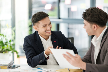 Smiling young businessman discussing something positive with his mature colleague, and using a digital tablet together