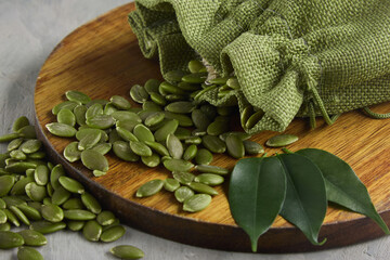 Wall Mural - On a round wooden board are scattered useful green pumpkin seeds from the bag. Raw pumpkin seeds for a healthy diet are beautifully laid out on a wooden stand along with the leaves