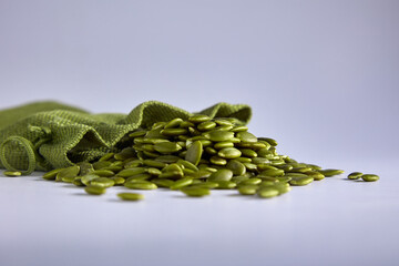 Wall Mural - Peeled raw healthy pumpkin seeds are poured out of the green bag. Pumpkin seeds on a gray background in a storage bag. Healthy healthy food snack