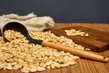 Wall Mural - On a wooden table, scattered roasted peanuts are collected in a bag with a long cook. On a gray background, dried peanuts are scattered from a bag on a brown kitchen table next to wooden utensils