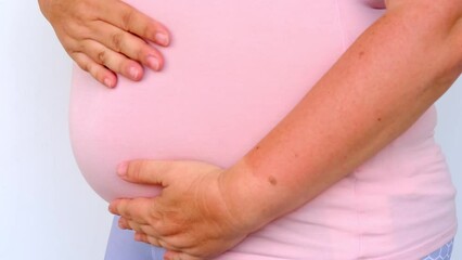 Poster - middle-aged pregnant woman in pink t-shirt holding her belly, waiting for newborn, concept of pregnancy reproduction, in vitro fertilization, planning late pregnancy after 40 years, selective focus