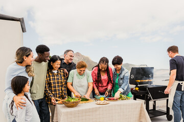 Multigenerational friends having fun doing barbecue at house rooftop - Happy multiracial people cooking together - Summer gatherings and food concept