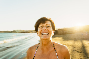 Happy Caucasian senior woman having fun smiling into the camera on the beach during summer vacation - Elderly people lifestyle concept