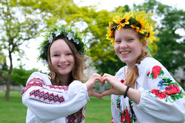 two girls girlfriends make hands one heart laughs smile Ukrainian vyshyvankas national emblems wreaths on their heads spring summer joy autumn entertainment Victory family reunion Ukrainian smile