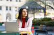 © Maria Vitkovska - Portrait of beautiful pensive Indian woman using laptop computer, planning project looking away waiting someone on the street. Asian student studying in university campus using wireless internet