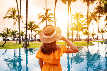 Young female relaxing and looking beautiful sunset over the sea at a tranquil tropical beach resort on summer vacation