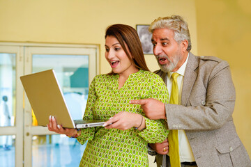 Senior businessman giving happy expression after looking in laptop with female colleague.