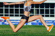 close-up female athlete jumping triple jump in summer athletics championships on background green field