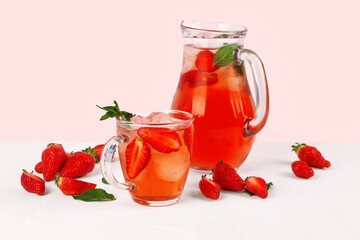 Glass cup and jug of tasty strawberry drink on white background