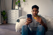 © StratfordProductions - Young biracial man in casual clothing using mobile phone for banking in bedroom at home