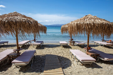 Wall Mural - Straw umbrella on wooden pole, lounger on sandy beach. Sunny day sea sky. Greece, Cyclades island.