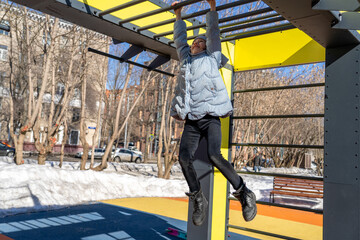 Child girl playing, hanging and climbing on bar on playground, outdoor exercise. Kids sport. Spring outdoors activity. Workout for children at playground. Kid exercise in park.  Healthy lifestyle.