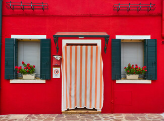 Wall Mural - Door and window with flower on the red facade of the house. Colorful architecture in Burano island, Venice.