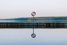 Lifebuoy Reflection On Lake, Trees In Background