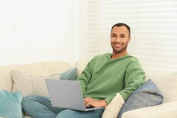 Sticker - Smiling African American man with laptop on sofa in room