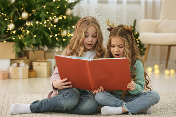 Poster - Cute little girls reading book at home. Christmas atmosphere