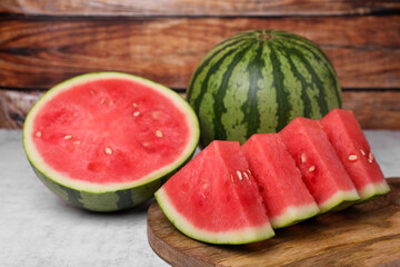 Wall Mural - Juicy ripe cut and whole watermelons on white table, closeup