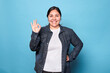 Young curvy latina woman wearing denim shirt and hoop earrings, smiling showing okay sign, hand on waist, looking at camera isolated on blue background. Copy space.