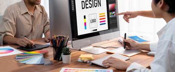 Fototapete - Graphic designer work on computer laptop and with graphic drawing pen while brainstorming unique design with professional graphic team in modern digital studio workplace. Panorama shot. Scrutinize