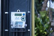 Digital electricity meter on pole. Electric meter showing energy consumption in high precision figures mounted on high voltage poles with blurred background of trees and houses. selective focus
