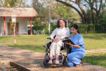 Wall Mural - Asian nurse or physiotherapist caring for elderly woman sitting wheelchair. Asian female nurse takes care of patients and takes them for a walk in the hospital park.