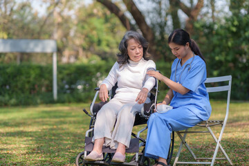 Wall Mural - Asian nurse or physiotherapist caring for elderly woman sitting wheelchair. Asian female nurse takes care of patients and takes them for a walk in the hospital park.