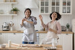 © fizkes - Cheerful adult daughter and excited mature mom in cooking aprons dancing at kitchen table with baking ingredients, laughing, having fun, enjoying music, movement, family culinary activity