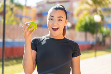 Wall Mural - Young pretty brunette woman with an apple at outdoors with surprise and shocked facial expression