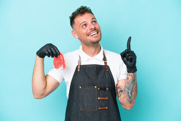 Wall Mural - Butcher caucasian man wearing an apron and serving fresh cut meat isolated on blue background pointing up a great idea