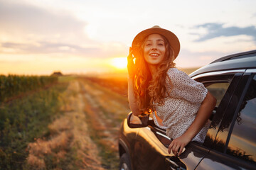 Wall Mural - Young woman is resting and enjoying sunset in the car. Woman on the road trip. ifestyle, travel, tourism, nature, active life.