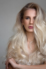 Wall Mural - Portrait of a young blonde woman with lush wavy hair. Gray background