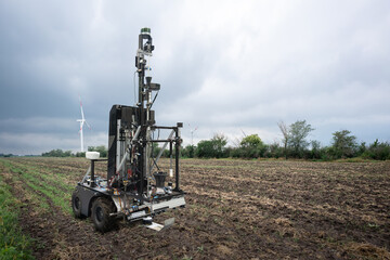 Fototapete - Autonomous robot for measuring soil quality in an agricultural field. Wind turbine on a horizon. Smart farming concept