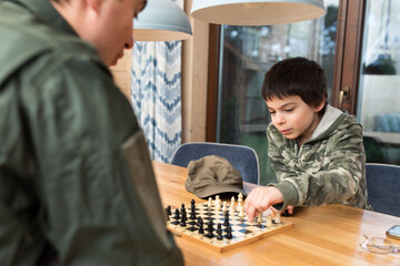 Wall Mural - Little adorable boy playing chess with his father in military uniform at home