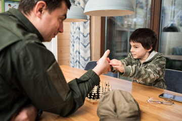 Wall Mural - Military man in olive uniform playing chess and having fun with his little son at home