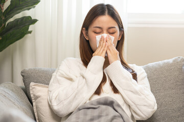 Wall Mural - Sick, coronavirus or covid-19, attractive asian young woman, girl have a fever, flu and hand in use tissues paper sneezing nose, runny while sitting on sofa, couch at home. Health care on virus person