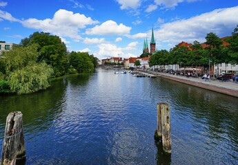 Canvas Print - Scenic view of the tranquil Trave river surrounded by traditional buildings and greenery in Germany