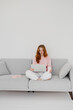 © Olena Bloshchynska - Beautiful young redhead woman using laptop, sitting on couch at home.