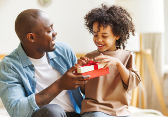 Wall Mural - Happy Fathers day. African american kid son giving  gift box to dad for holiday at home