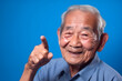 Asian grandfather looking and smiling with rised index finger on blue background. Neural network generated in May 2023. Not based on any actual person, scene or pattern. Generative AI