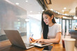 © dodotone - Business freelance asian woman using laptop and writing note work at coffee cafe table