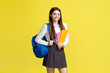 © Maria Vitkovska - Portrait of smiling teenage girl wearing school uniform, blue backpack, looking at camera isolated on yellow background. Back to school