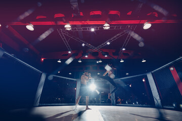 Boxers fighter finishes off enemy in MMA ring octagon, dark background spot light