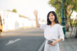 © Jirawatfoto - Portrait young beautiful asian woman waving hand to friend by the street in sunny holiday.