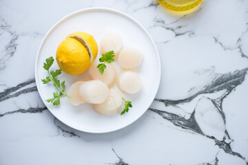 Wall Mural - Fresh uncooked sea scallops with lemon and parsley, flat lay on a black and white marble background, horizontal shot, copy space