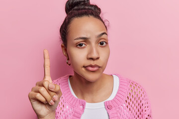 Canvas Print - Serious attentive Latin woman got idea or solution has excellent plan in mind keeps index finger raised uo looks self confident dressed casually isolated on pink background. Hey listen me attentively