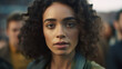 © wetzkaz - young adult woman with short curly brunette hair outdoors in a city wearing a jacket, people in the background. fictional place